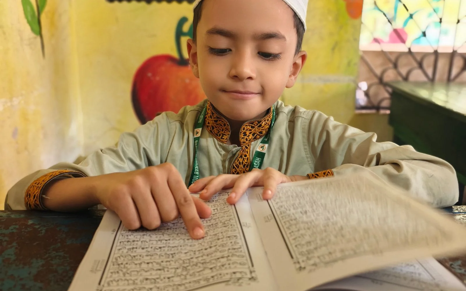 Young boy reading Arabic text at his desk while learning Quranic Arabic