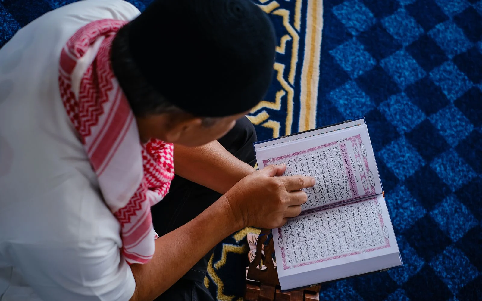 Man reciting from a Quran on a wooden rehal, following each line