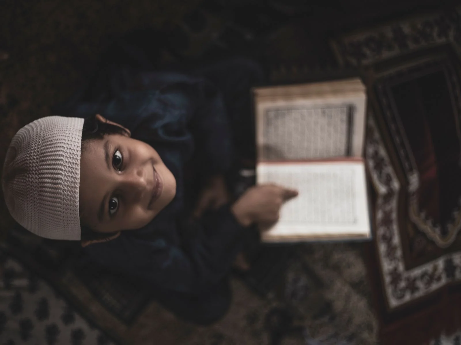 Smiling young boy reading the Quran on a prayer mat
