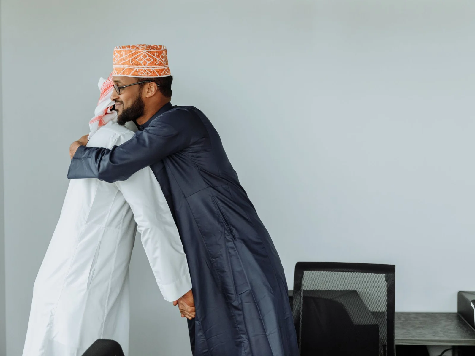 Two Muslim men in traditional dress embracing warmly