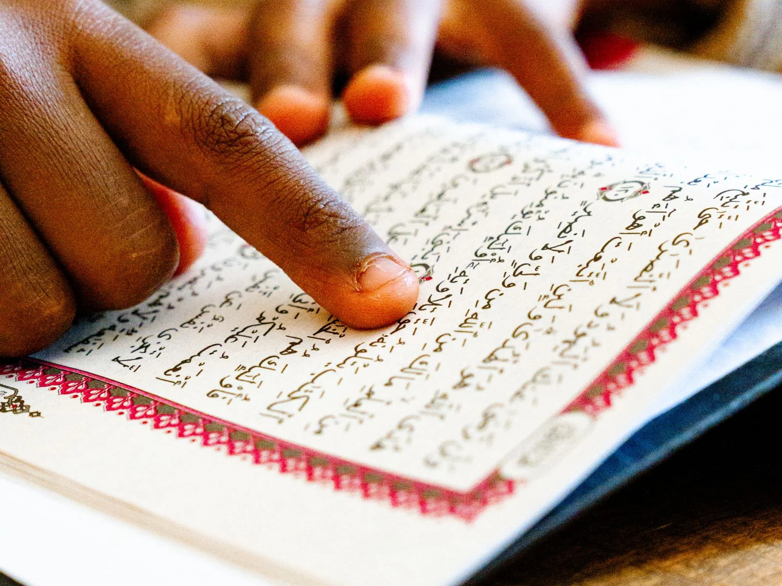 Finger pointing to Arabic letters on a Quran page