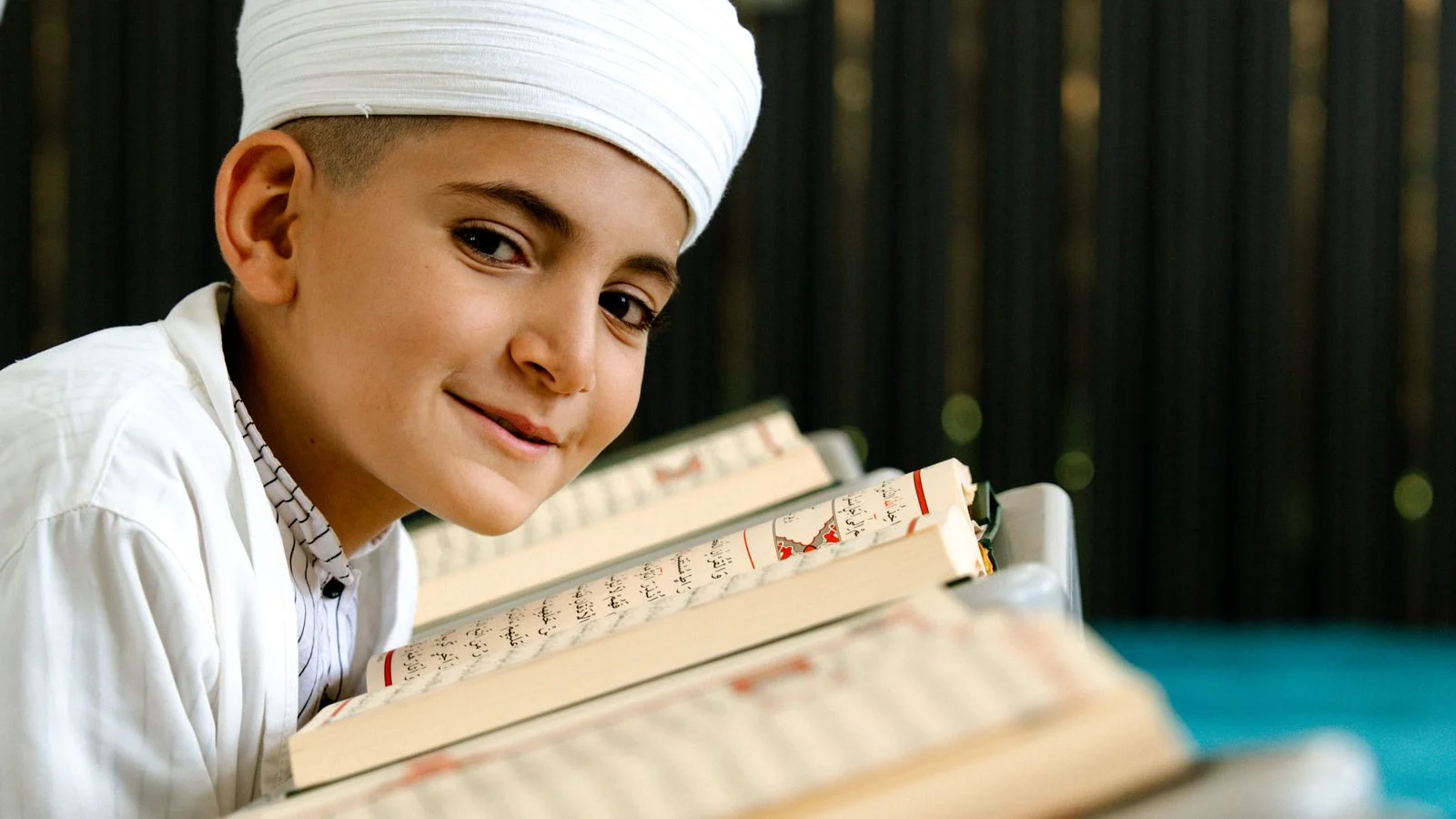 Smiling young boy holding the Quran during a Noorani Qaida lesson
